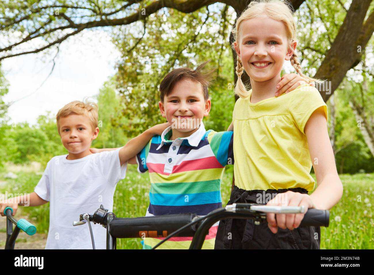 Portrait d'une fille souriante debout par des amis masculins avec des vélos dans le parc pendant les vacances d'été Banque D'Images Portrait d'une fille souriante debout par des amis masculins avec des vélos dans le parc pendant les vacances d'été Banque D'Images