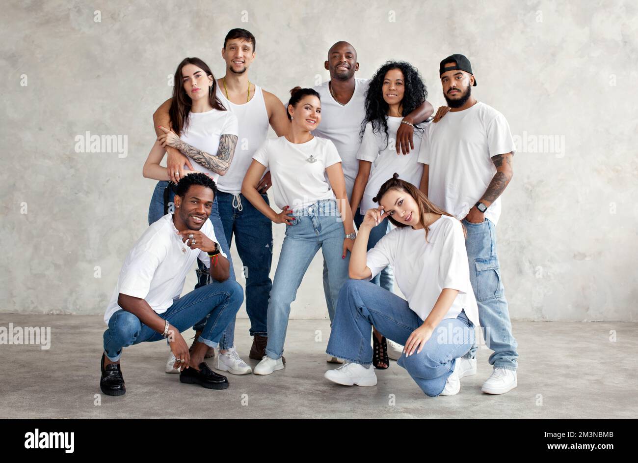 Groupe multiethnique d'amis heureux. Divers jeunes se tenant ensemble dans des chemises blanches et des jeans sur fond minimaliste en studio Banque D'Images