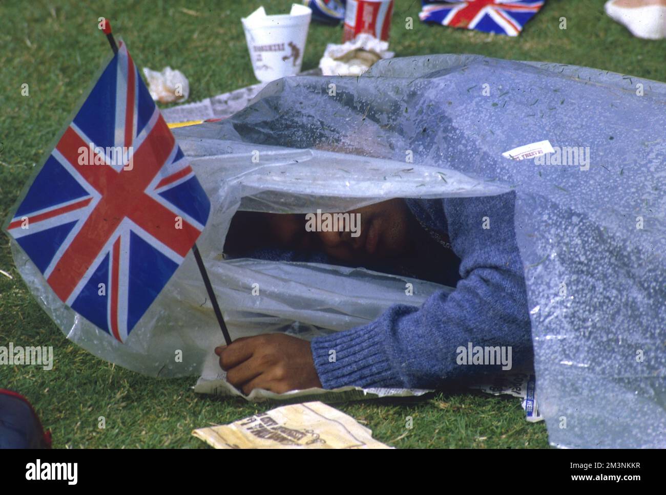 Un homme dort sous une feuille de plastique alors qu'il sécurise son terrain d'observation pour assister au mariage du prince Andrew, du duc de York et de Sarah Ferguson le 23 juillet 1986. Patriotique même dans le sommeil, il saisit d'une main un drapeau de l'Union Jack. 1986 Banque D'Images