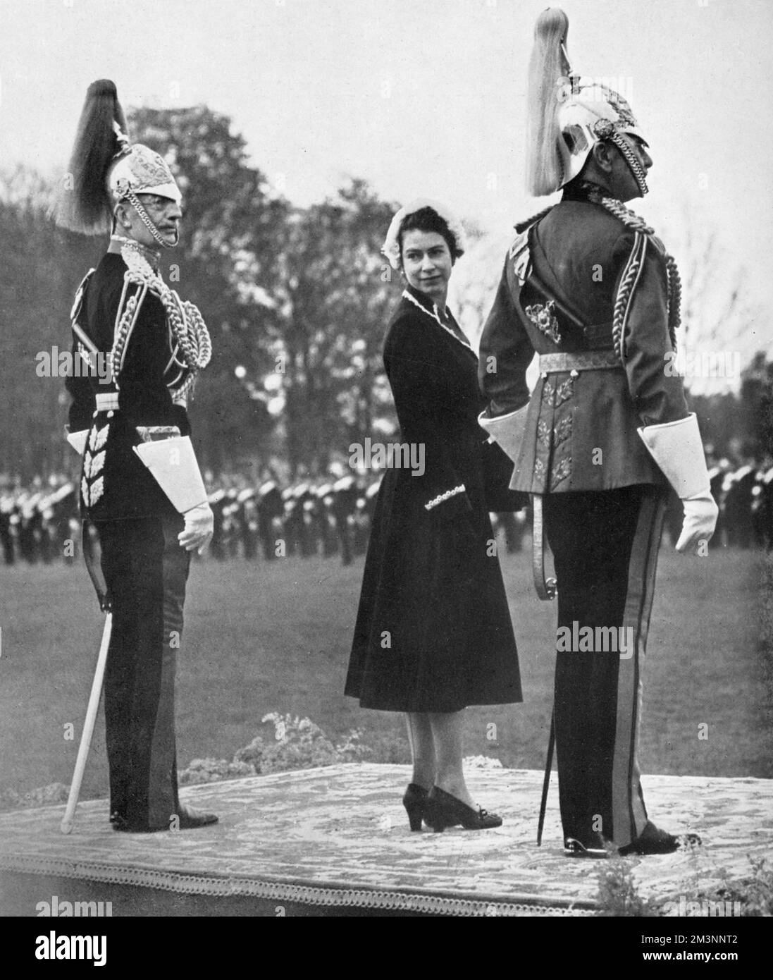 Une jeune reine Elizabeth II regarde de nouveau par-dessus son épaule pendant qu'elle attend une parade de la cavalerie de la maison à Home Park, Windsor, au cours d'une présentation de nouvelles normes. Elle est flanquée du colonel de la Royal Horse Guards, du Maj-Gen Sir Richard Howard-Vyse et de son arrière-oncle, l'honorable Maj-Gen, le comte d'Athlone. Date: 1953 Banque D'Images