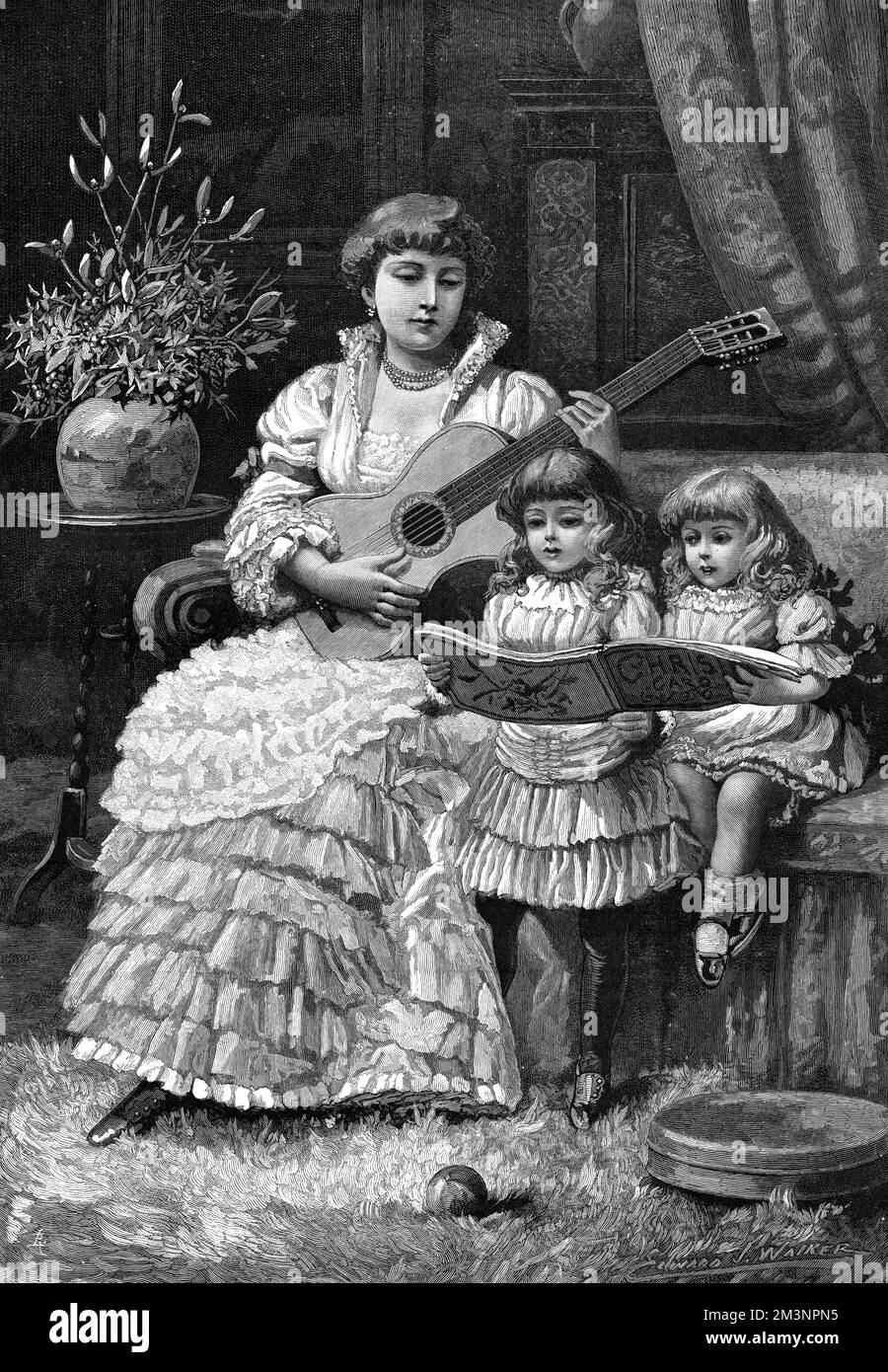 Une femme assise sur un canapé joue de la guitare tandis que deux petites filles chantent des chants de Noël à partir d'un livre de musique. Un peu de houx et de GUI dans un vase complètent la scène festive. Date: 1885 Banque D'Images