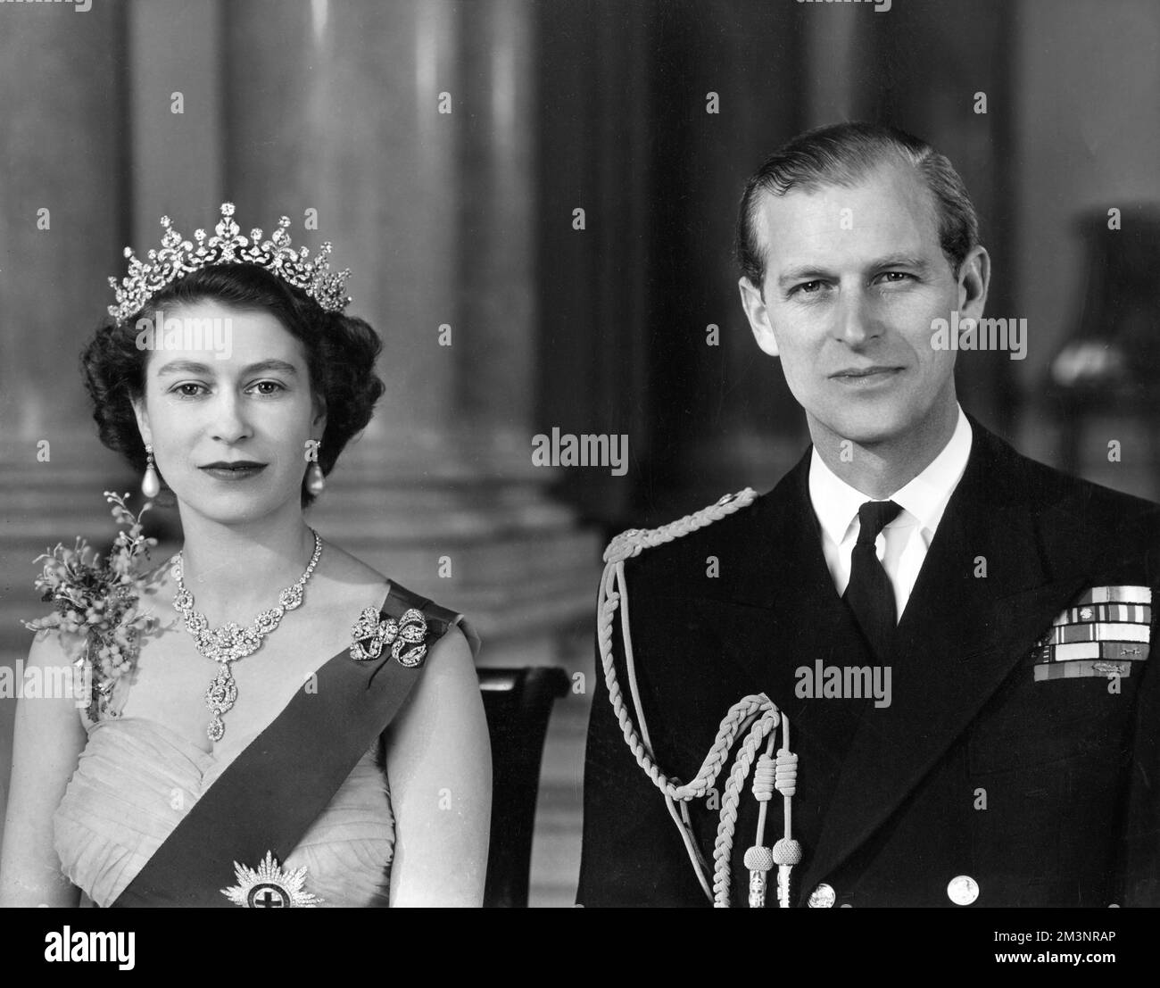 La reine Elizabeth II et le prince Philip, duc d'Édimbourg photographiés ensemble à l'entrée principale du palais de Buckingham en 1954. La Reine porte une robe de soirée en tulle jaune ornée de jets de mimosa et de broderie de pailette d'or et porte le ruban bleu et l'étoile de la jarretière. Son collier était un cadeau de mariage du Nizam de Hyderabad; le tiara était également un cadeau de mariage de la reine Marie. La broche en forme de noeud et les pendants d'oreilles sont ornés de diamants. Le duc porte l'uniforme de l'amiral de la flotte. Date: 1954 Banque D'Images