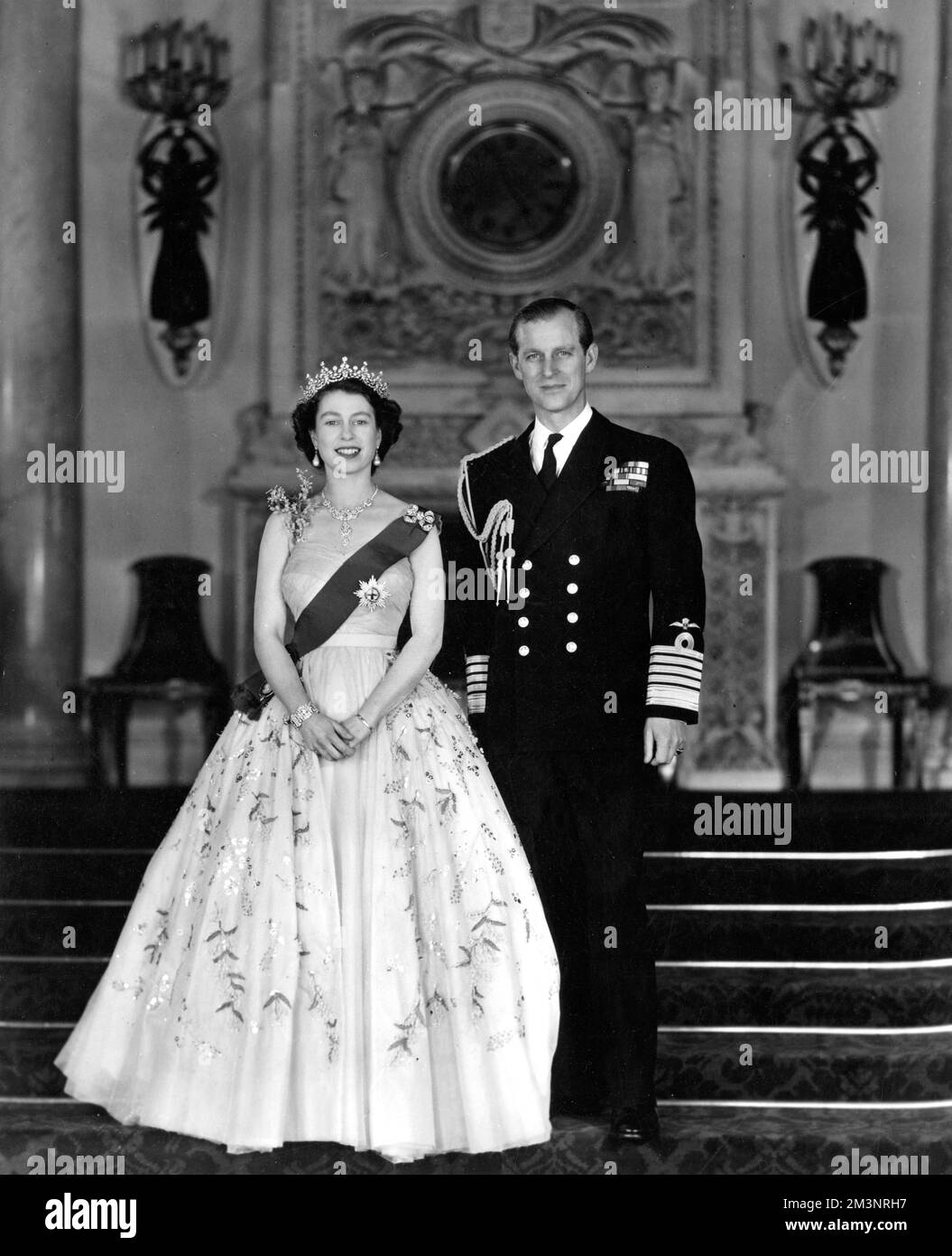 Portrait de commandement Royal par le baron la Reine et le duc d'Édimbourg représenté à l'entrée Grand du Palais de Buckingham, la Reine est vue dans une robe de soirée en tulle jaune ornée de jets de mimosa et de broderie de paaillette dorée : elle porte le ruban bleu et l'étoile de la jarretière. Ce sont quelques détails de ses diamants Majestys présentés dans le portrait. Le collier est un cadeau de mariage du Nizam de Hyderabad; le tiara, également un cadeau de mariage, de la reine Marie. La broche d'arc, les pendants d'oreilles, le bracelet et la montre-bracelet en platine sont également en diamants. Le duc d'Édimbourg est Banque D'Images