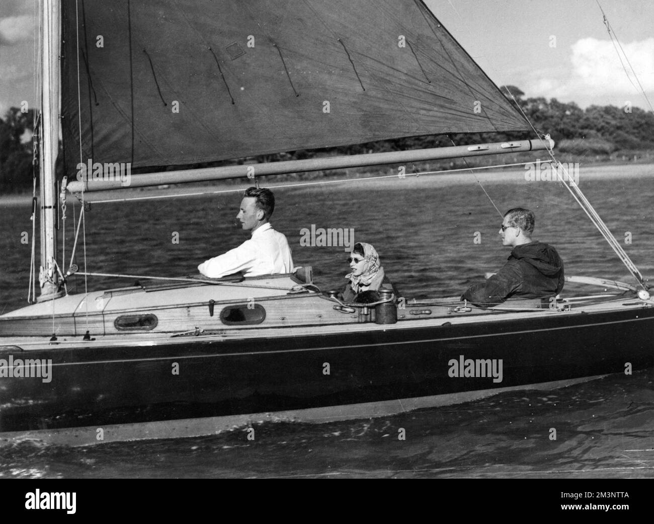 La reine Elizabeth II (alors que la princesse Elizabeth est toujours) regarde le prince Philip, duc d'Édimbourg à la barre de son yacht, Bluebottle, dans la rivière Beaulieu, en face de Cowes. Date: 1949 Banque D'Images