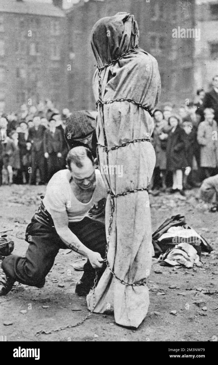 Un évatologue est préparé par son assistant pour une autre représentation, divertissant la foule au marché de Petticoat Lane, Londres, un dimanche matin Date: 1945 Banque D'Images