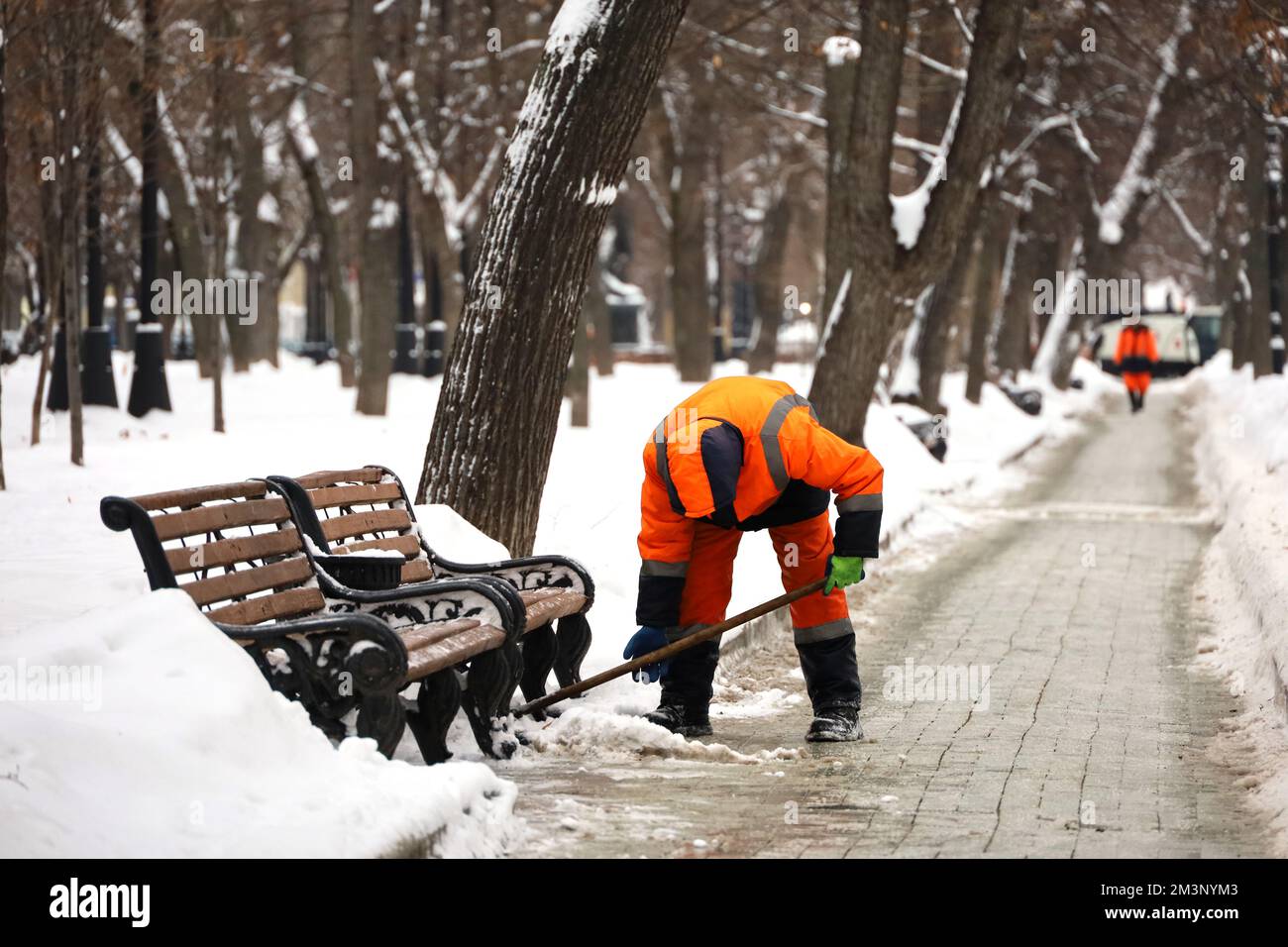 Un employé nettoie la neige dans les rues de la ville après une chute de neige. Homme avec une pelle dans le parc d'hiver Banque D'Images