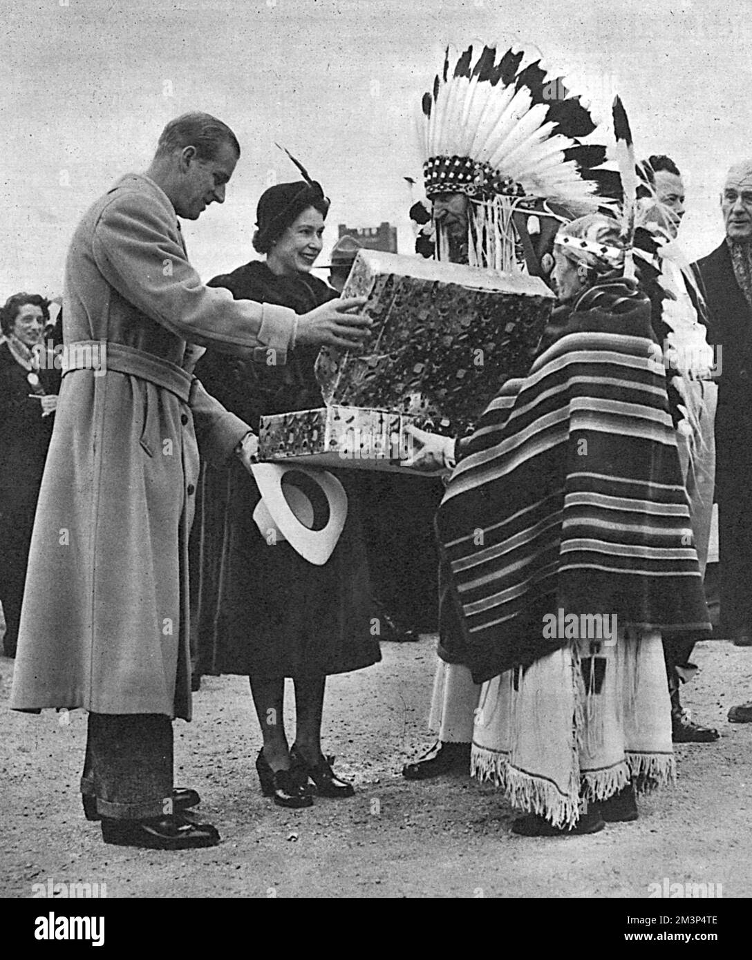 À Winnipeg, lors de la tournée royale du Canada, la princesse Elizabeth et le prince Philip reçoivent un cadeau pour la princesse Anne. Le cadeau est un petit costume amérindien, fait par Mme Antoinette HeavyShield, vu ici le présenter au nom de toutes les mères des cinq peuples amérindiens du sud de l'Alberta. Au centre se trouve le chef Percy Creighton, qui agit comme interprète. Date : octobre 1951 Banque D'Images