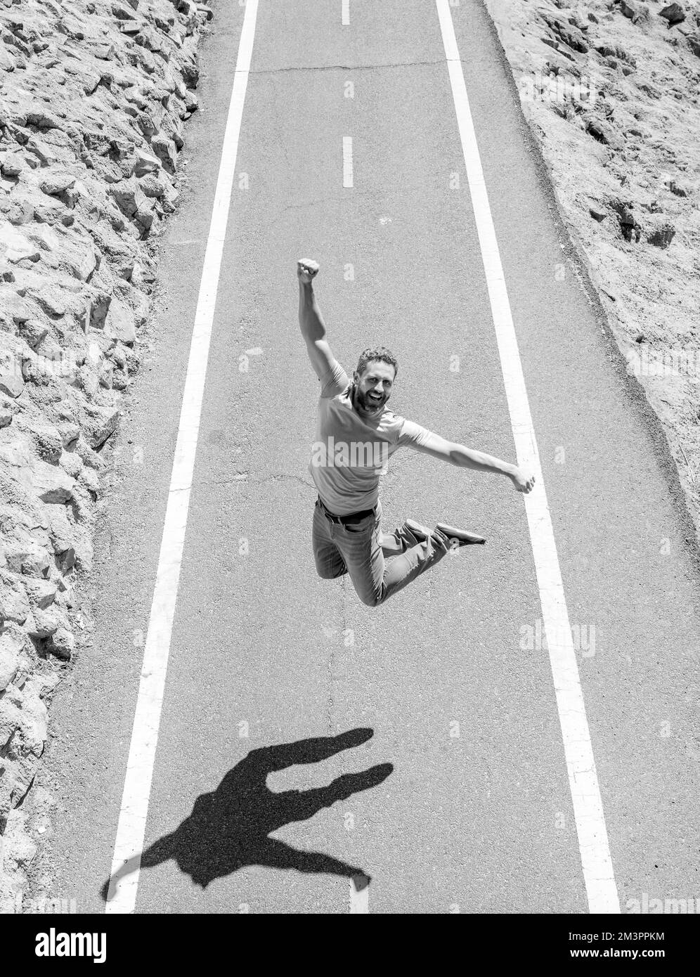 joyeux homme d'athlétisme mûr sautant sur la route en plein air, motivation Banque D'Images