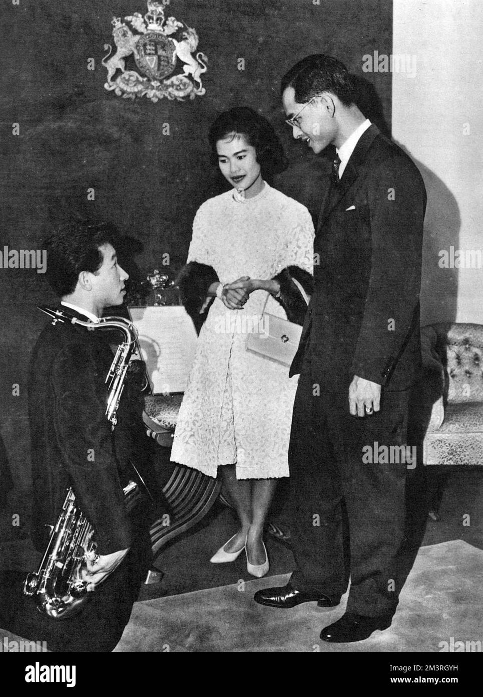 Une visite officielle de l'Australie par le roi Bhumibol Adulyadej (Rama IX) (1927-) et la reine Sirikit (1932-) de Thaïlande. Le couple royal reçoit l'hommage d'un étudiant thaïlandais, M. D. Juejok, à Sydney, en Nouvelle-Galles du Sud. Le Roi, un musicien prend le temps d'avoir une conversation avec le saxophoniste à genoux, qui venait de jouer l'hymne national thaïlandais. Date: 1962 Banque D'Images