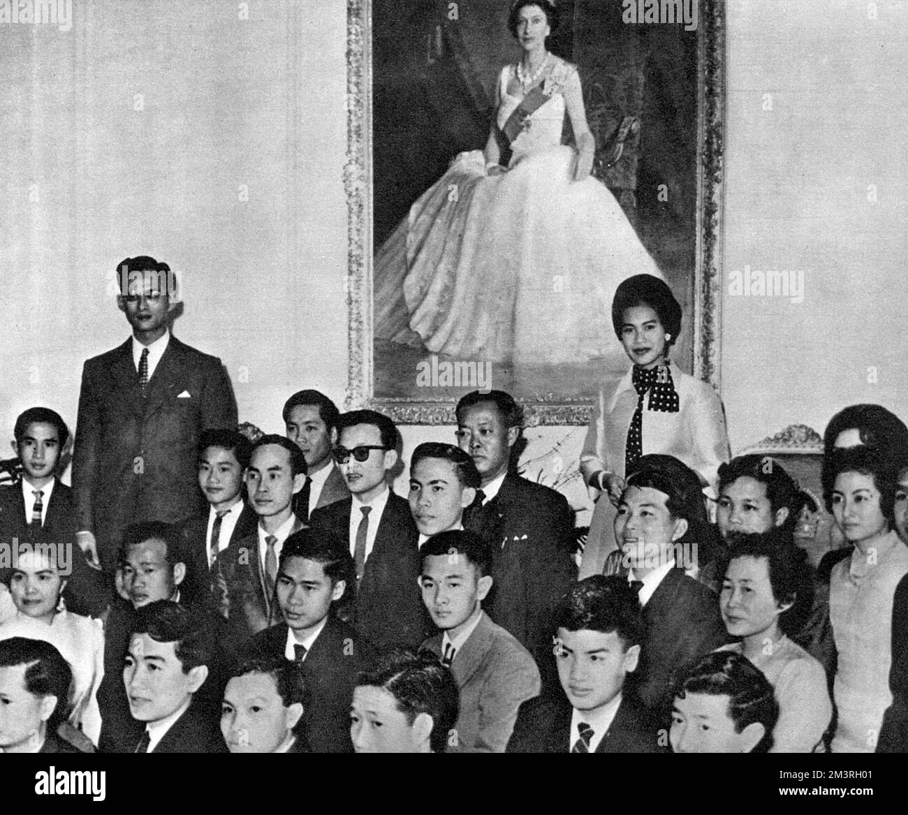Une visite officielle de 8 jours en Nouvelle-Zélande par le roi Bhumibol Adulyadej (Rama IX) (1927-) et la reine Sirikit (1932-) de Thaïlande - photo prise à la Maison du gouvernement, Wellington, alors qu'un grand groupe d'étudiants thaïlandais se réunissent autour du roi et de la reine, sous un portrait complet de la reine Elizabeth II Date: 1962 Banque D'Images