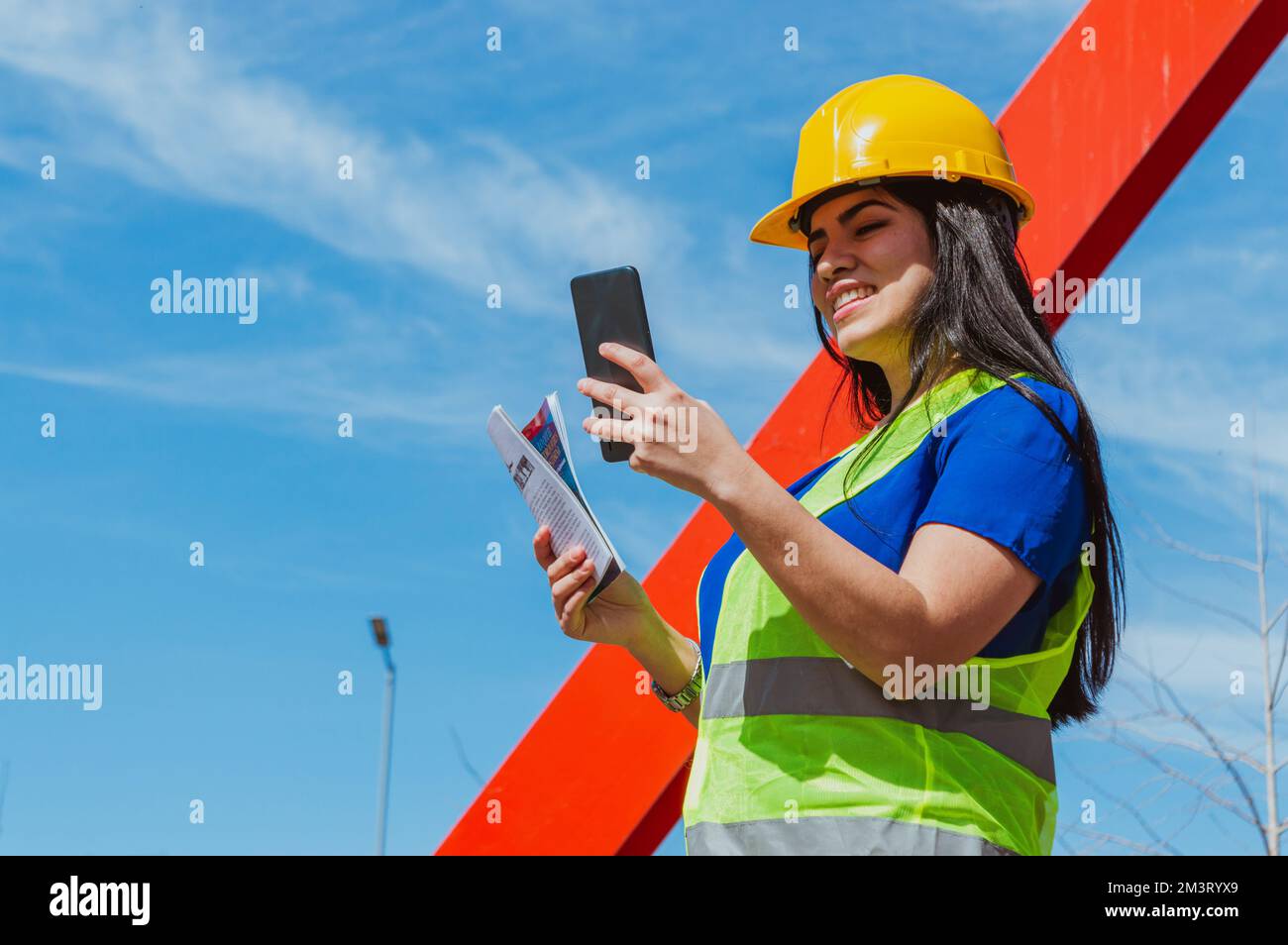 Caucasien jeune Latina ingénieur femme, travailleur dans un chantier de construction est heureux souriant et de vérifier son téléphone à l'extérieur, l'espace de copie. Banque D'Images