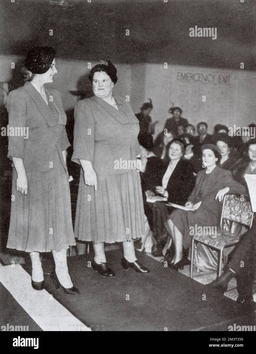 Mme Bessie Braddock (à droite) dans son rôle de "grand reine de la mode". Bessie Braddock (1899 - 1970), députée travailliste de la Liverpool Exchange Division, avec Mlle Elizabeth Fry, qui présente la même robe modèle à l'affichage de mode grand format Dorchester à Londres, 1951. Mme Braddock est en demande pour ouvrir des défilés de mode de grande taille. Ses commentaires sont toujours piqueux, comme en témoigne sa déclaration : « J'aime une robe que quelqu'un avec des hanches décentes peut porter. » Sur les jeux de couleurs, elle dit : « vous êtes toujours bien en bleu marine ». Elle a décrit le nouveau look comme « le caprice ridicule des personnes inactives ». Date: 1951 Banque D'Images