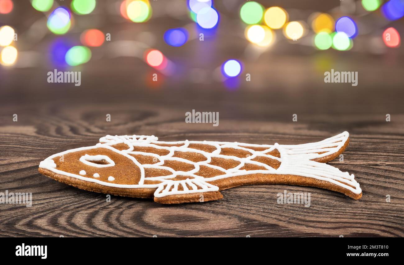Gros plan du biscuit de pain d'épice de Noël en forme de poisson sur fond de bois. Pâtisserie douce et aromatique pour les fêtes de Noël et le nouvel an. Lumières À DEL. Bokeh. Banque D'Images