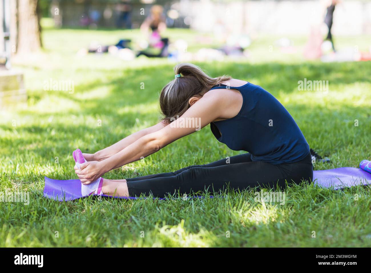 Une femme qui mène un mode de vie sain se rend dans le parc pour des sports, effectue un exercice pour étirer les muscles de ses jambes et de son dos Banque D'Images