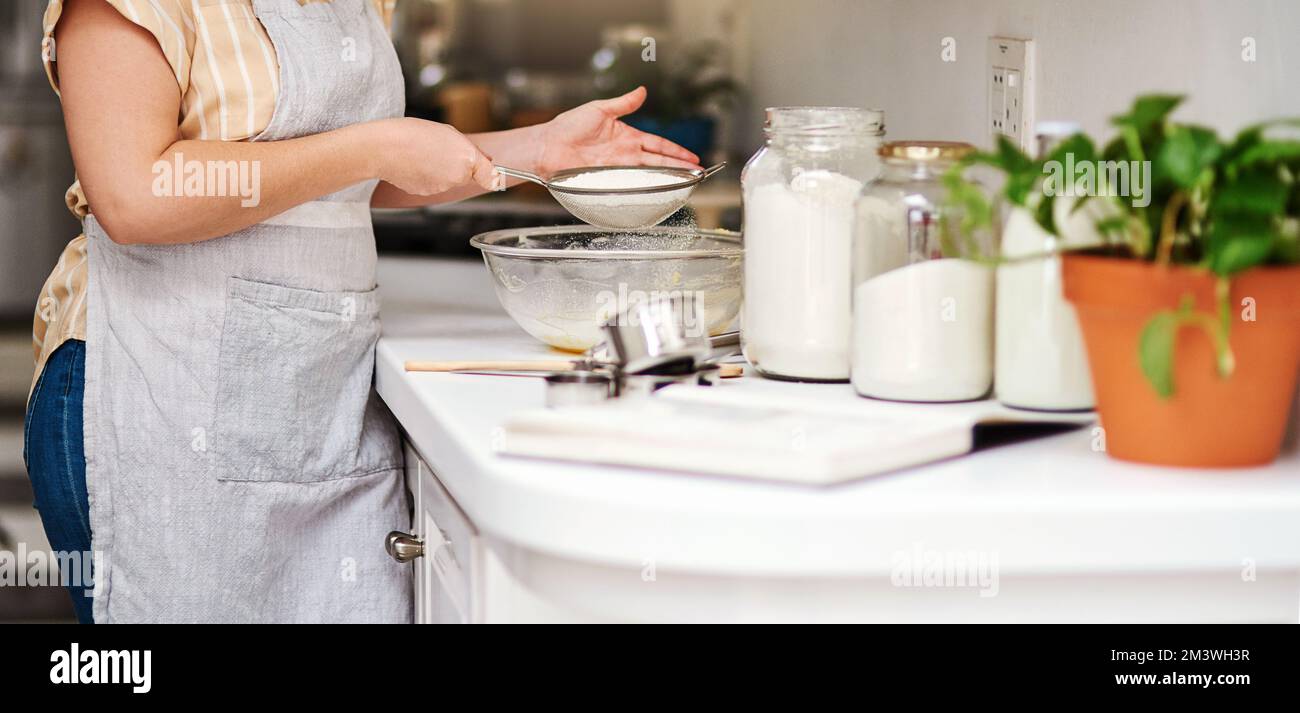 Pour l'amour de la pâtisserie. une femme tamisant de la farine dans un bol en verre. Banque D'Images