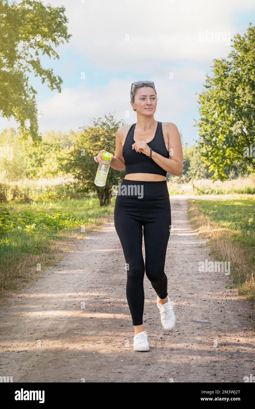 Jeune belle femme en uniforme noir jogging dans le parc d'été. Portrait horizontal. Banque D'Images