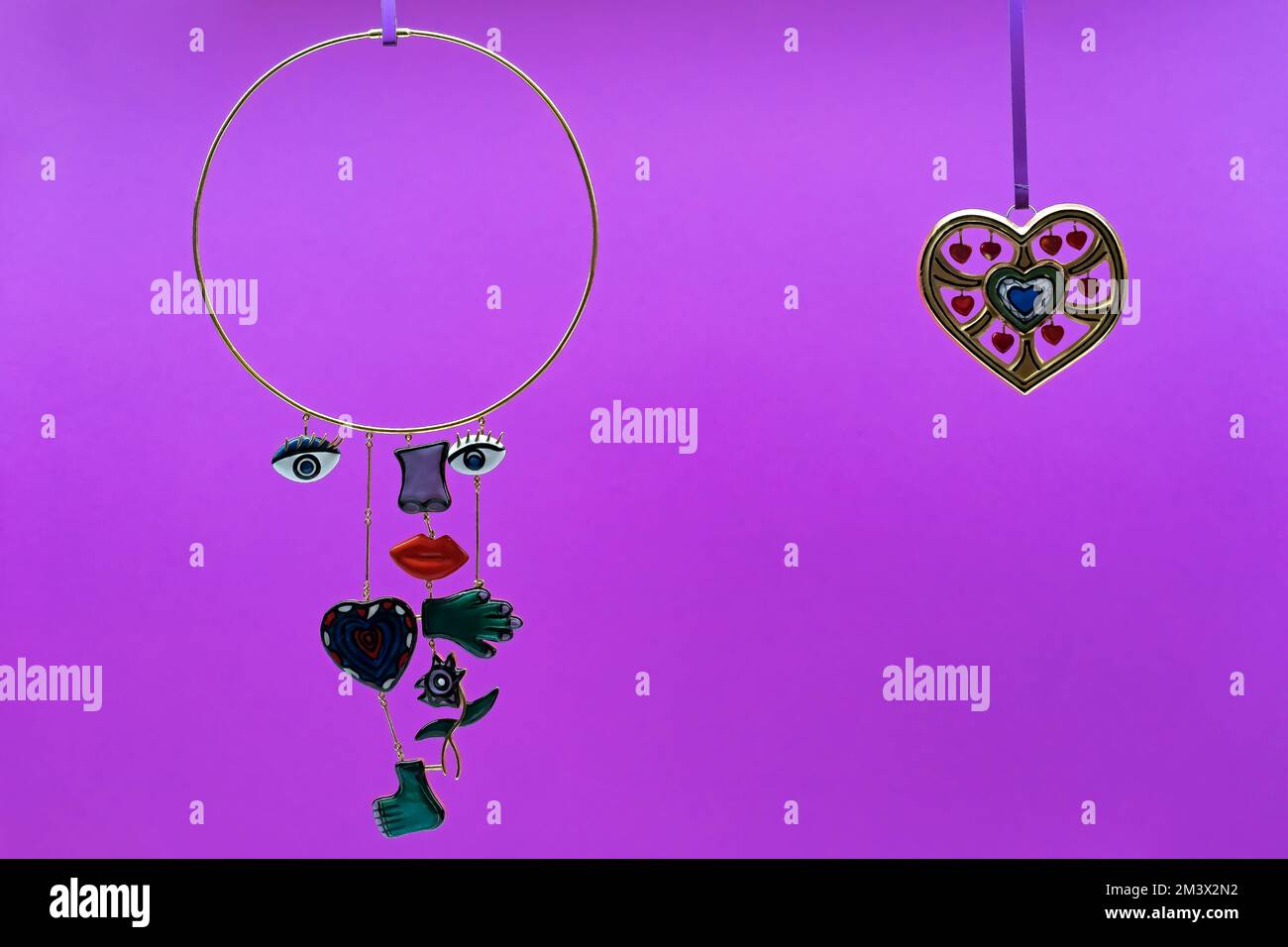 Collier or rond avec yeux, nez, bouche, coeur, main, pied, et fleur. Bijoux avec parties du corps disjointes sur fond violet électrique. Banque D'Images