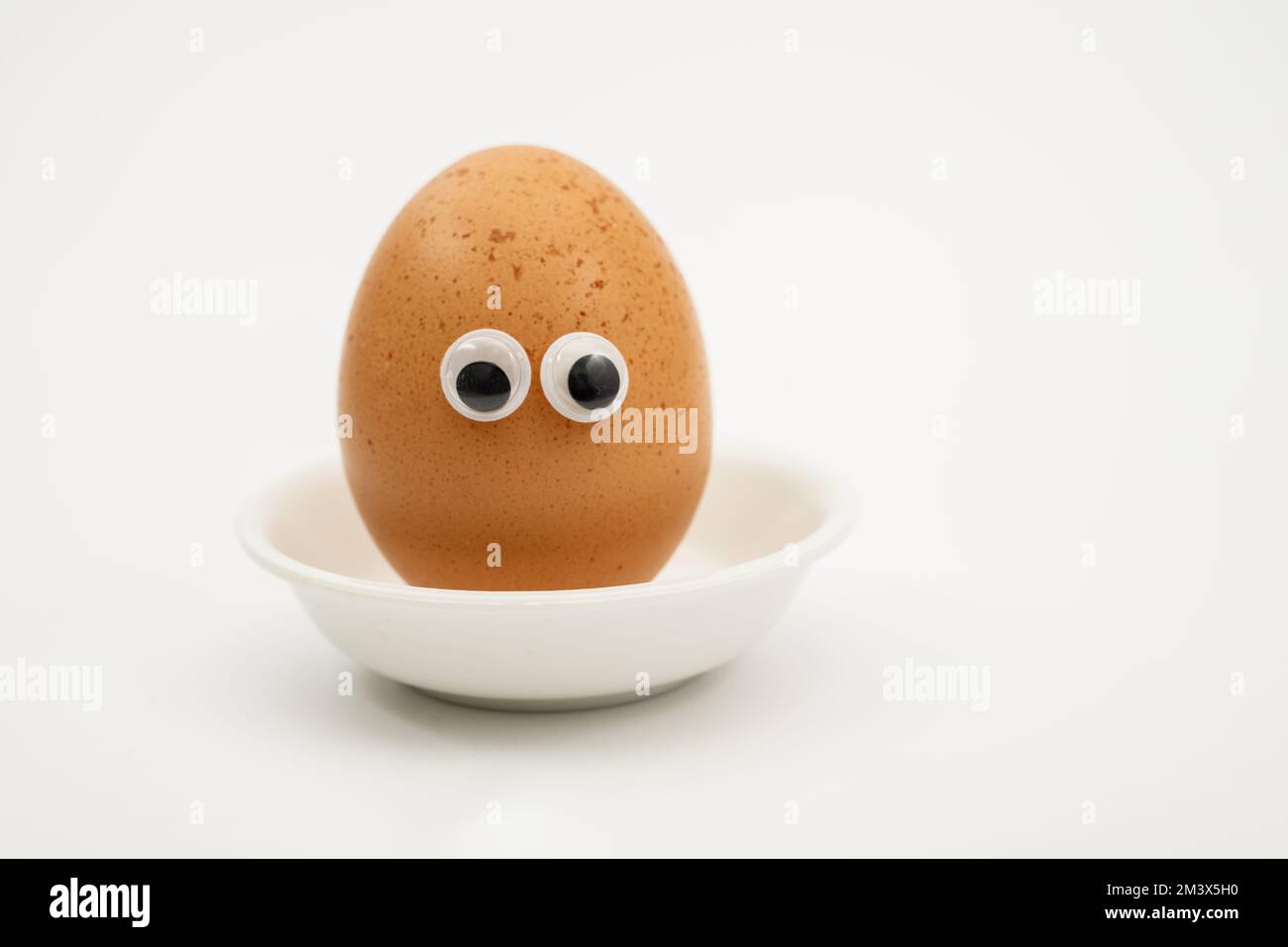 oeuf dur dans un support avec effet yeux de gogly pour petit déjeuner d'enfant isolé sur un fond blanc Banque D'Images