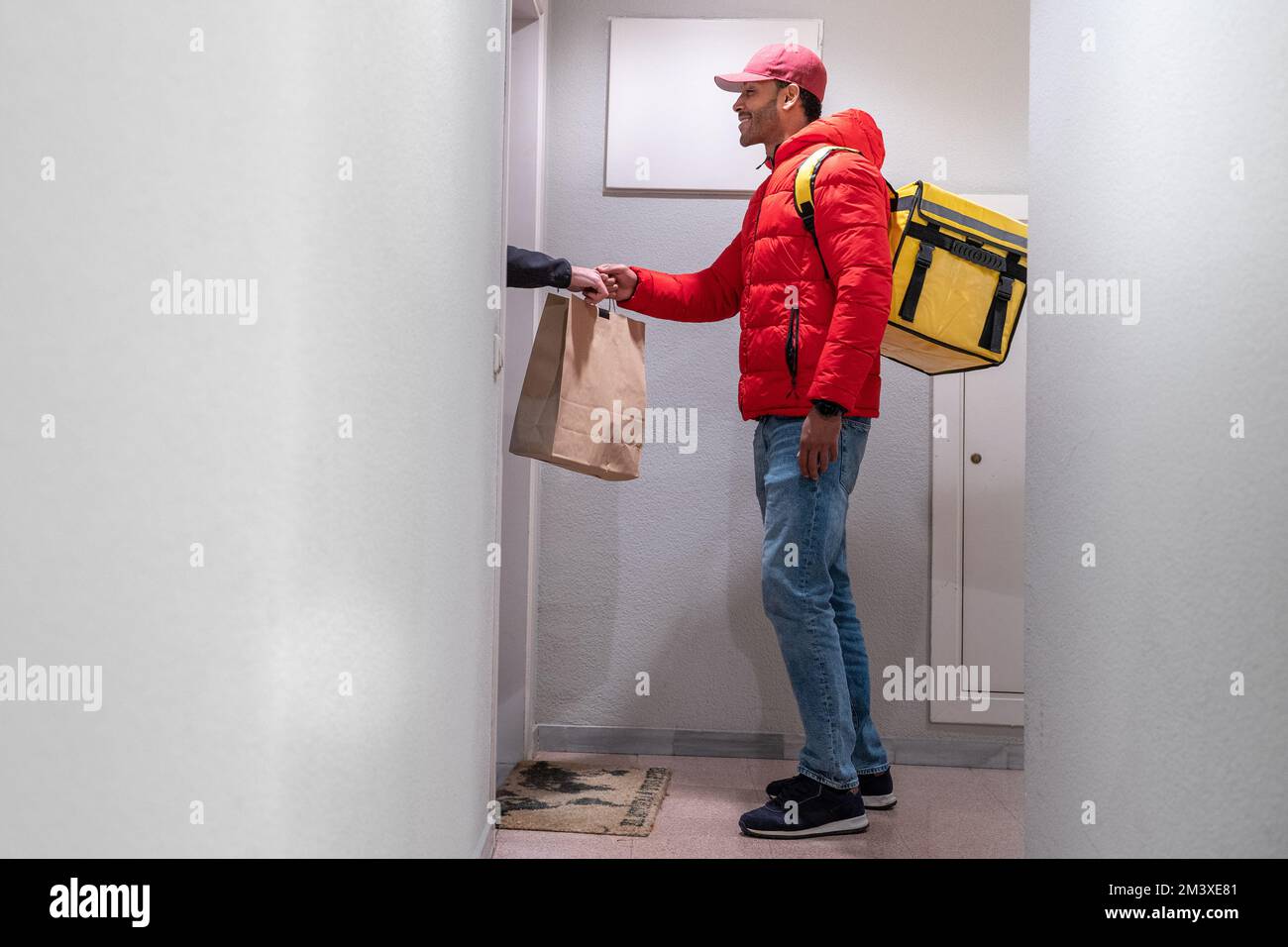 Concept de livraison de nourriture. Jeune Afro-américain souriant avec sac à dos qui livre des produits à la porte. Banque D'Images