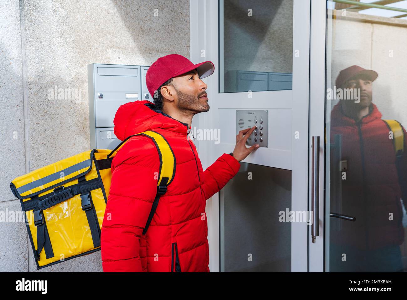 Travailleur américain africain de livraison de nourriture dans une porte frappant à la porte d'un immeuble d'appartements. Banque D'Images