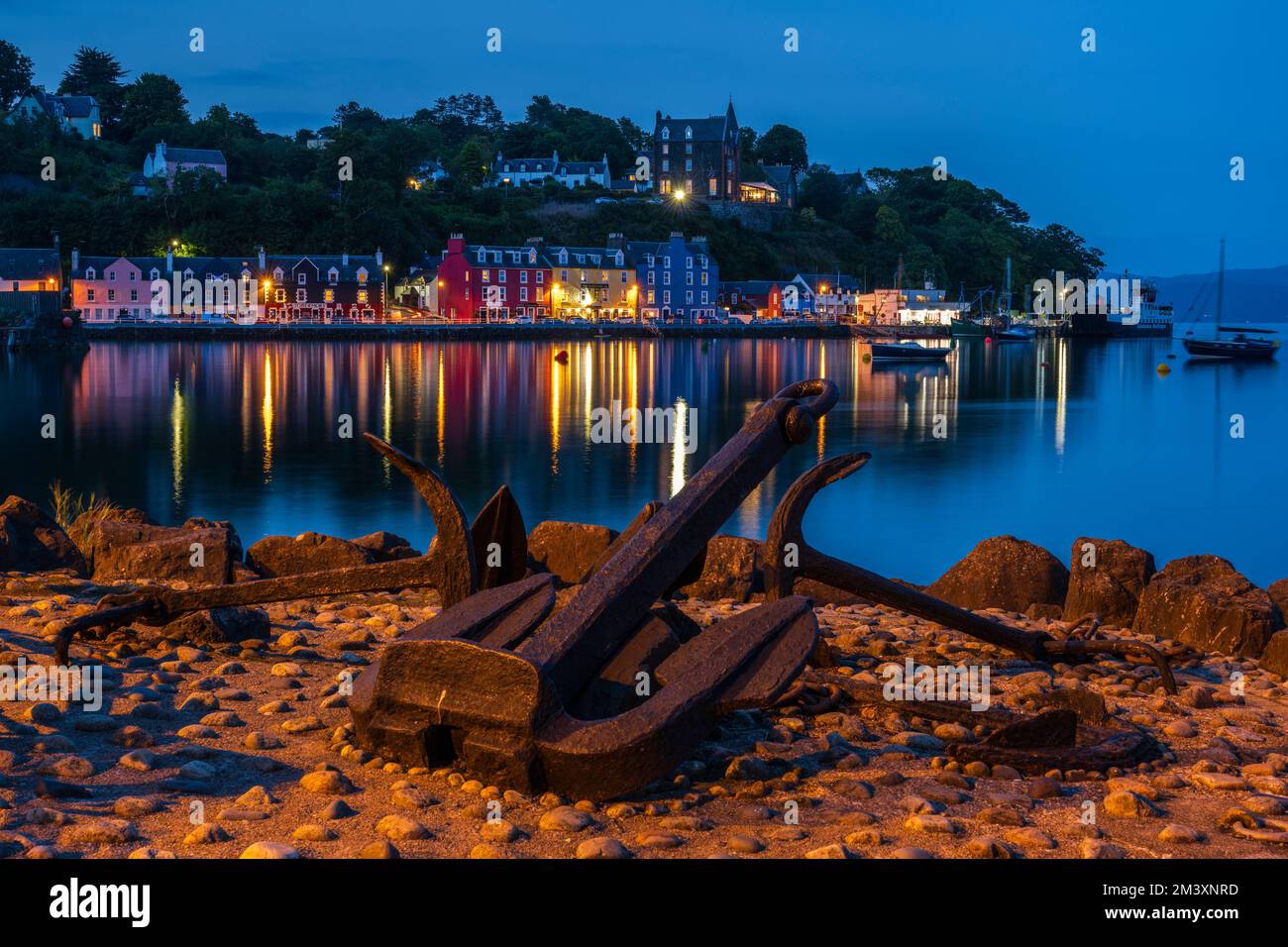 Ancres sur le quai avec les lumières colorées du front de mer reflétées dans l'eau encore du port de Tobermory, île de Mull, Écosse, Royaume-Uni Banque D'Images