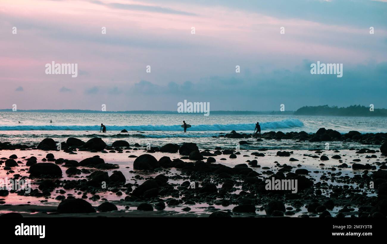 Les surfeurs se sont défait contre le coucher du soleil sur la plage de Medewi, à Bali. Banque D'Images