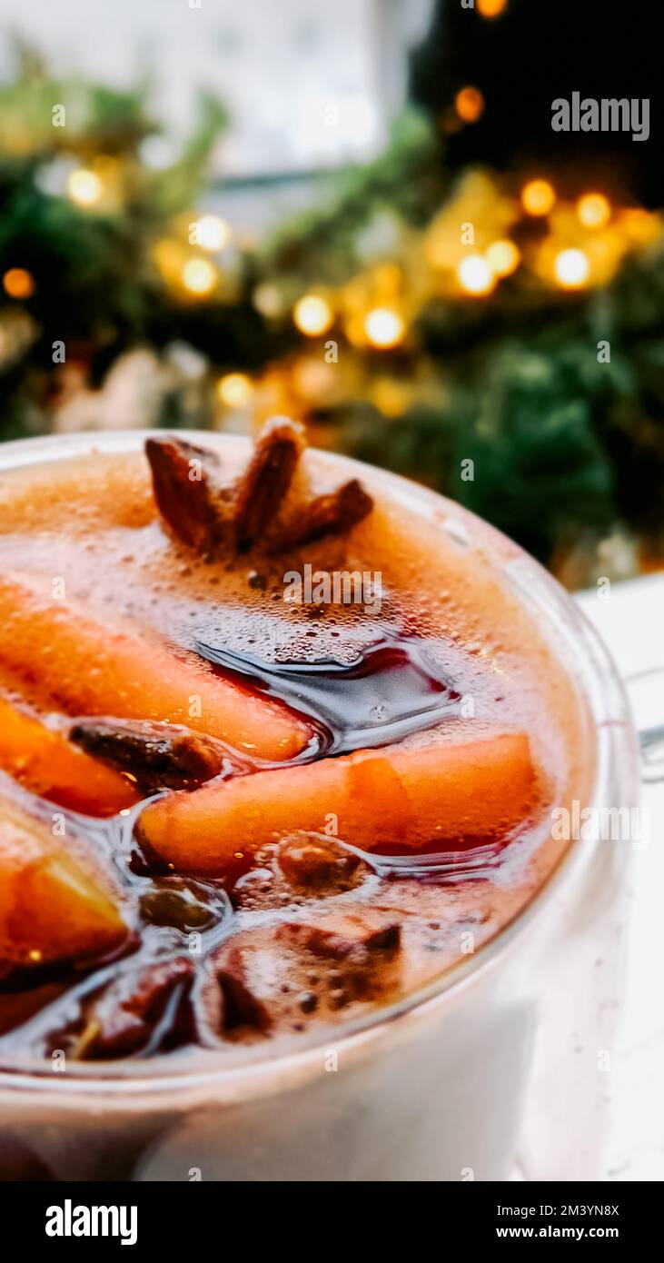 Vin chaud de Noël sur fond flou de lumières vives. Boisson chaude traditionnelle du nouvel an à base de vin rouge, d'orange, de cannelle, de pommes et d'épices anis étoilé. Cocktail de Noël. Mise au point sélective Banque D'Images