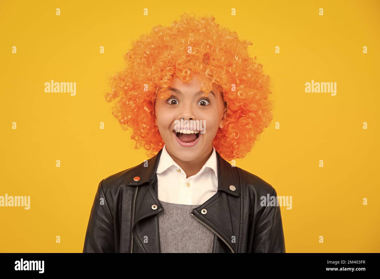 Fête d'anniversaire pour filles. Drôle d'enfant dans la perruque rouge curly. Temps de Amuse-toi bien. Jeune fille avec des cheveux orange, étant un clown. Visage excité, émotions gaies de Banque D'Images