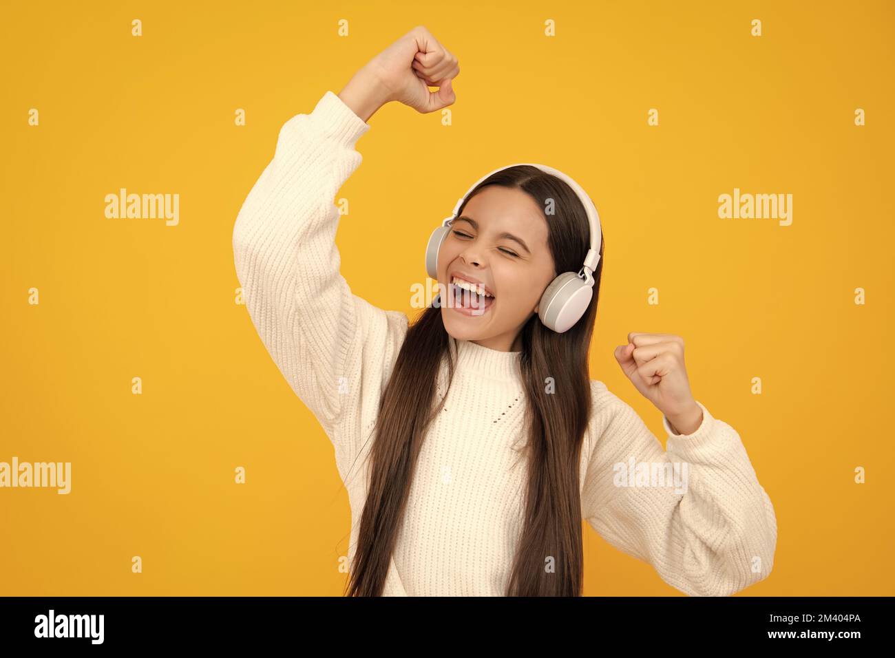 Visage excité. Une jeune fille dans un casque écoute de la musique. Accessoire de casque sans fil. L'enfant aime la musique dans les écouteurs sur fond jaune Banque D'Images