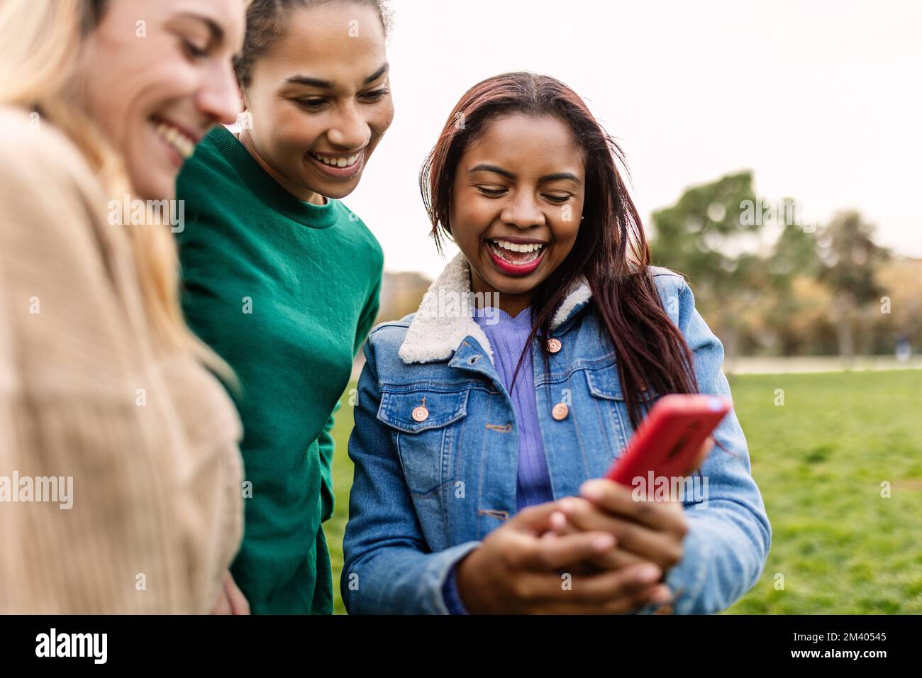Trois amies multiraciales tenant un téléphone mobile à l'extérieur Banque D'Images