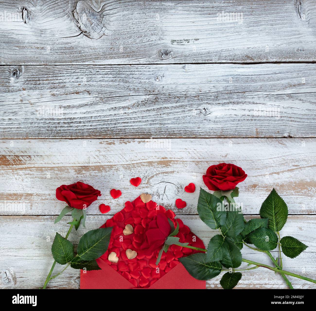 Concept de salutation de Saint-Valentin avec enveloppe remplie de petits coeurs dorés et rouges plus fleurs roses sur fond blanc rustique en bois Banque D'Images