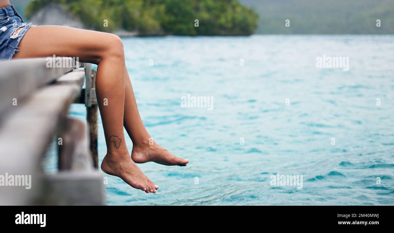 Rien de tel qu'un temps d'arrêt. une femme méconnaissable assise et pendante ses jambes sur le bord d'une promenade pendant les vacances. Banque D'Images