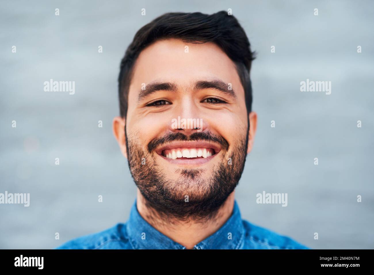 Juste un homme barbu insouciant. Gros plan portrait d'un beau jeune homme souriant debout contre un mur de briques. Banque D'Images