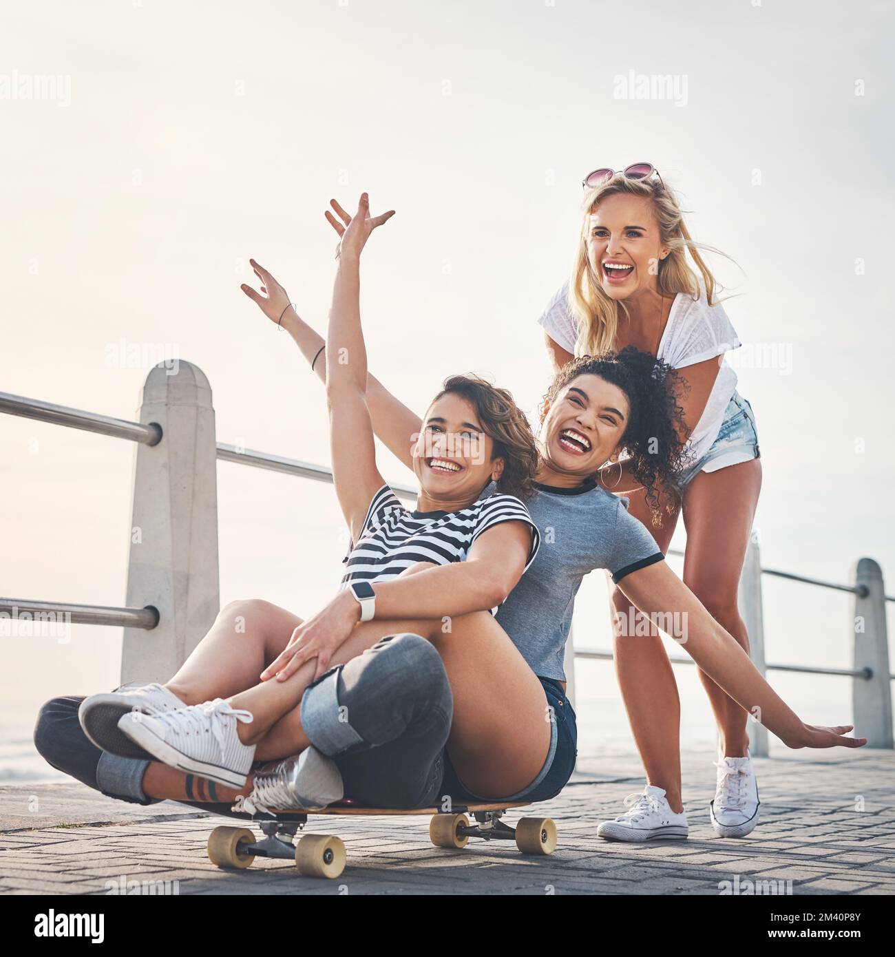 Nous rigolons jusqu'à ce que nos estomacs blessent. une femme poussant ses amis sur un skateboard pendant qu'elle est sur la promenade. Banque D'Images