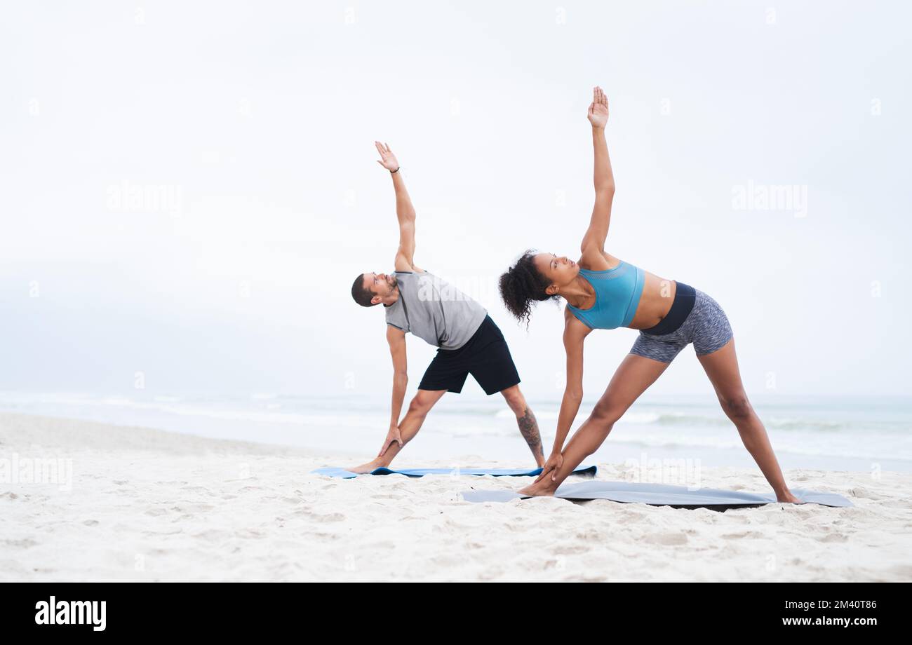 L'air frais nous inspire à garder la forme. un jeune homme et une jeune femme pratiquant le yoga ensemble à la plage. Banque D'Images