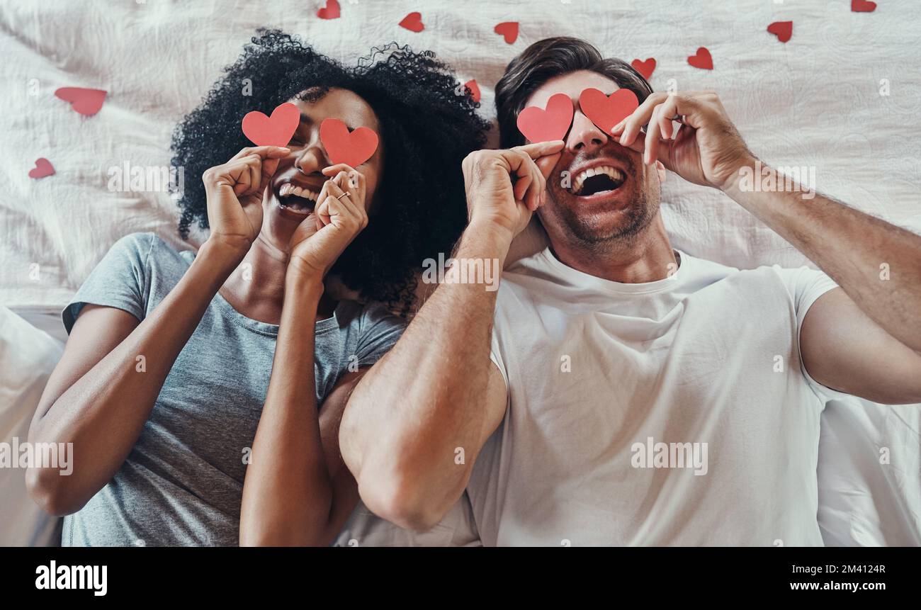 J'ai l'amour en vue. Photo en grand angle d'un jeune couple couvrant leur visage avec des décorations en forme de coeur dans leur chambre à la maison. Banque D'Images