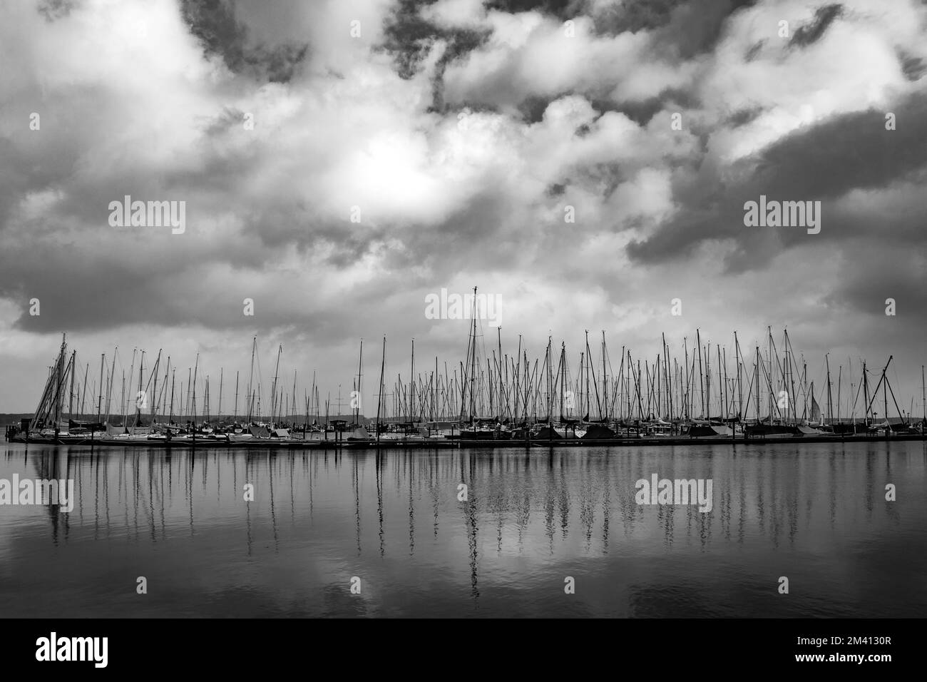 Une photo en noir et blanc d'un port avec des bateaux dans l'eau sur fond ciel nuageux Banque D'Images