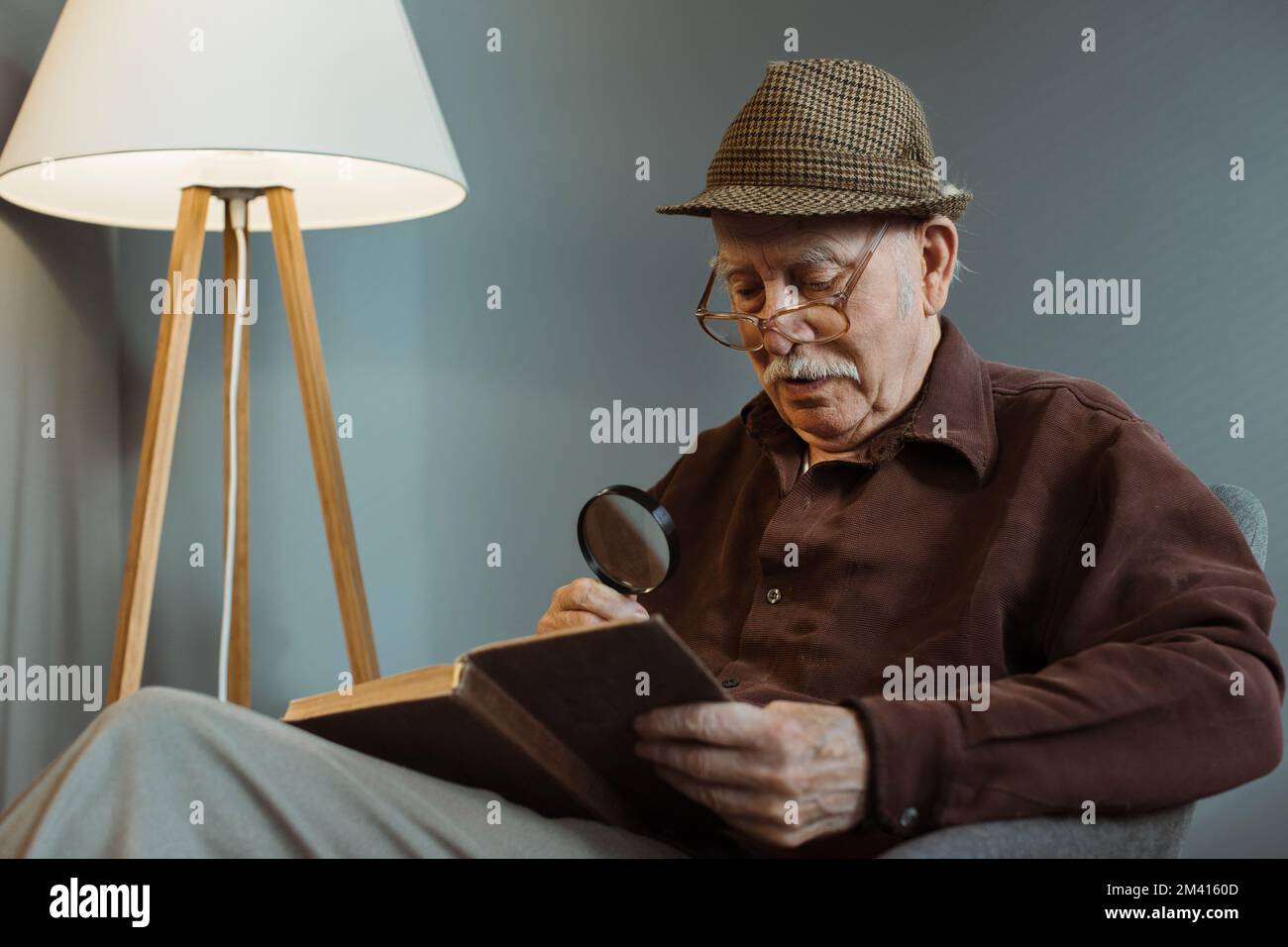 Un homme âgé est assis seul sur une chaise dans le salon, porte des lunettes et lit un livre. Banque D'Images