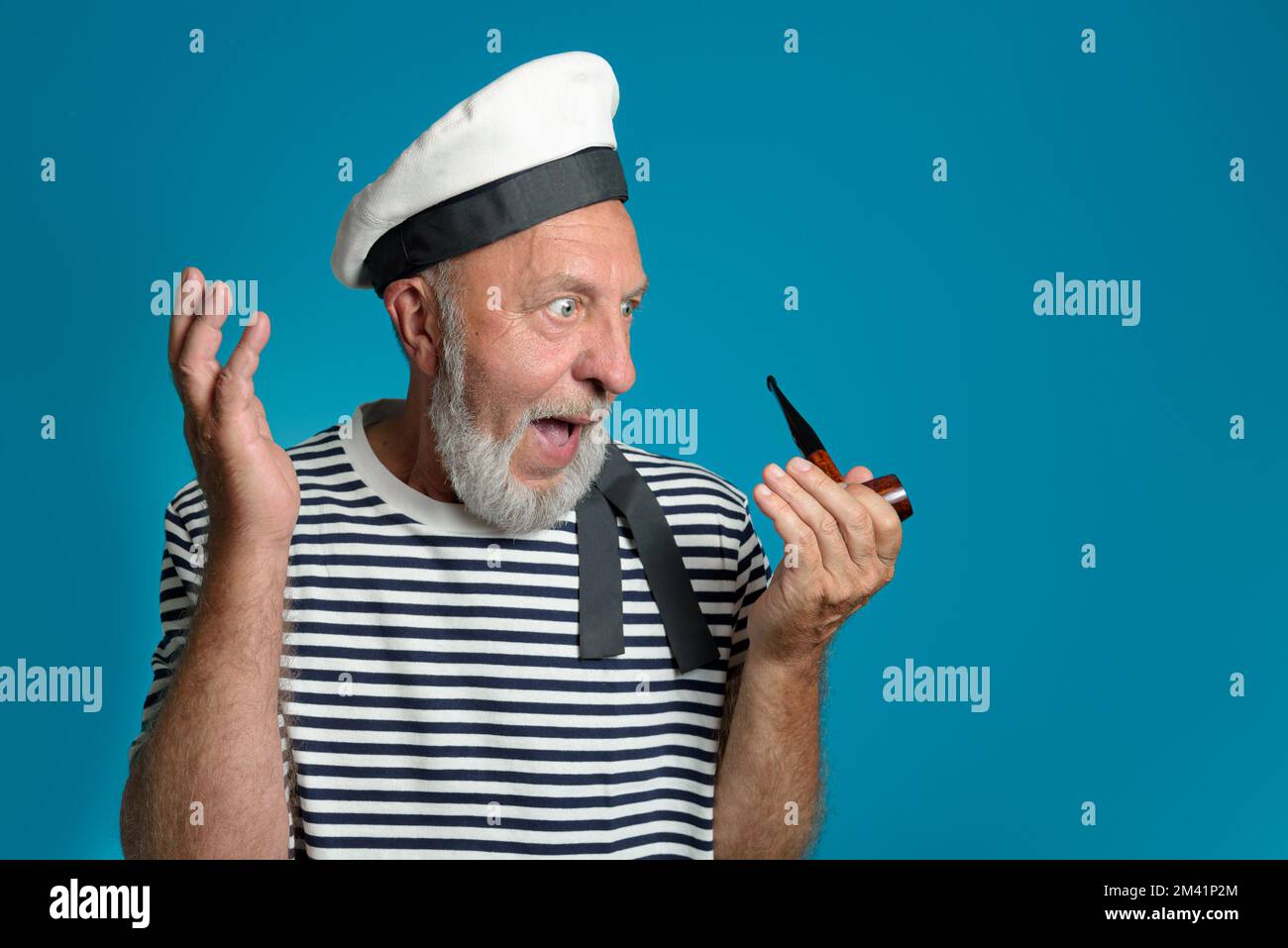 Génial. Vieux portrait de marin surprise et admiration. Tuyau de fumée, forme marine. sur un fond bleu isolé Banque D'Images