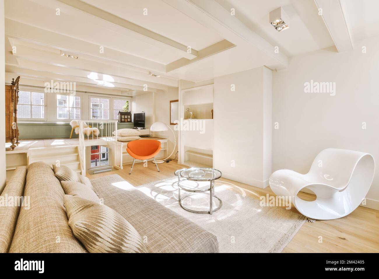 un salon avec des murs blancs et du parquet, il y a une chaise orange devant le canapé Banque D'Images