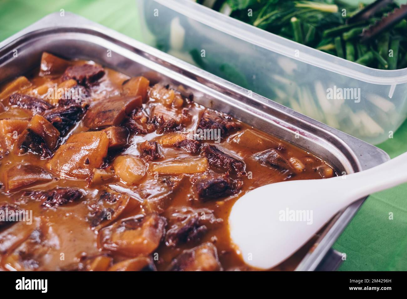 Délicieux ragoût d'Oxtail et de tripe philippin dans une sauce aux arachides riche et épaisse ou « Kare Kare » dans un plat de service en acier inoxydable en plus des légumes verts Banque D'Images