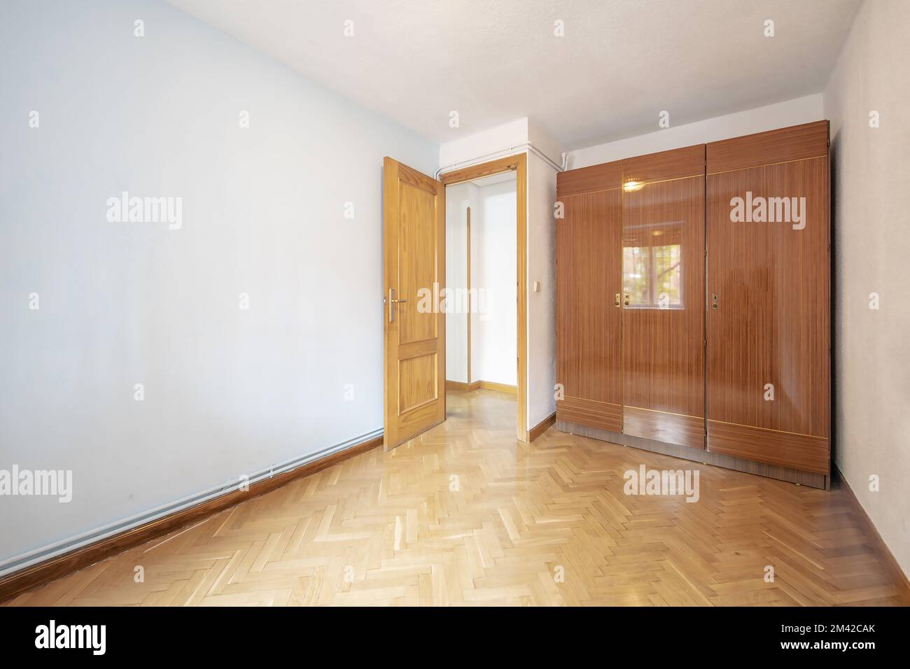 Une chambre vide avec une armoire avec trois sections de portes vernies brillantes avec parquet en chêne placé dans un motif à chevrons et des tuyaux d'eau chaude Banque D'Images