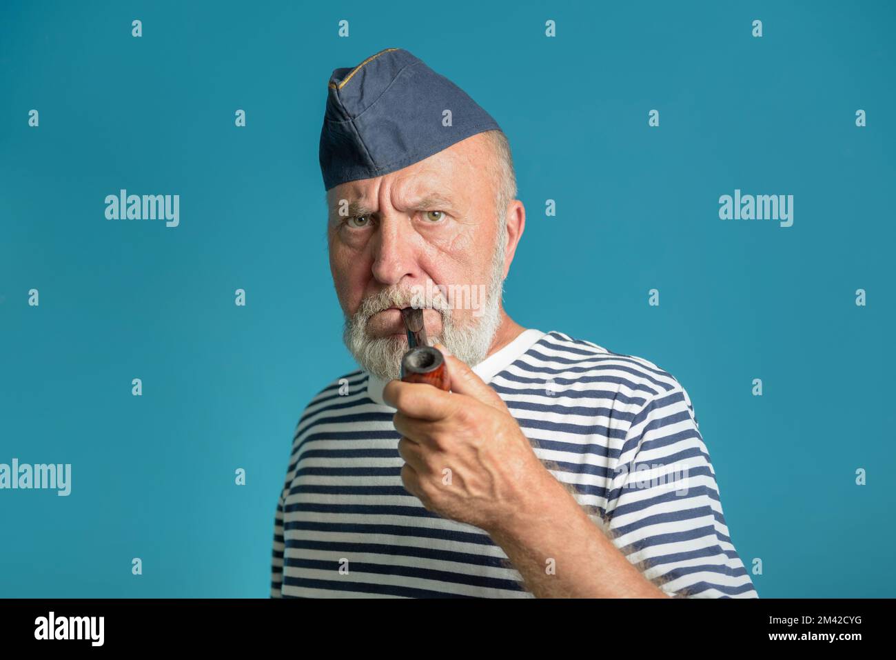 Un vieux marin avec un tuyau de fumée. Portrait d'un marin dans une chemise à rayures marine et une casquette bleue Banque D'Images