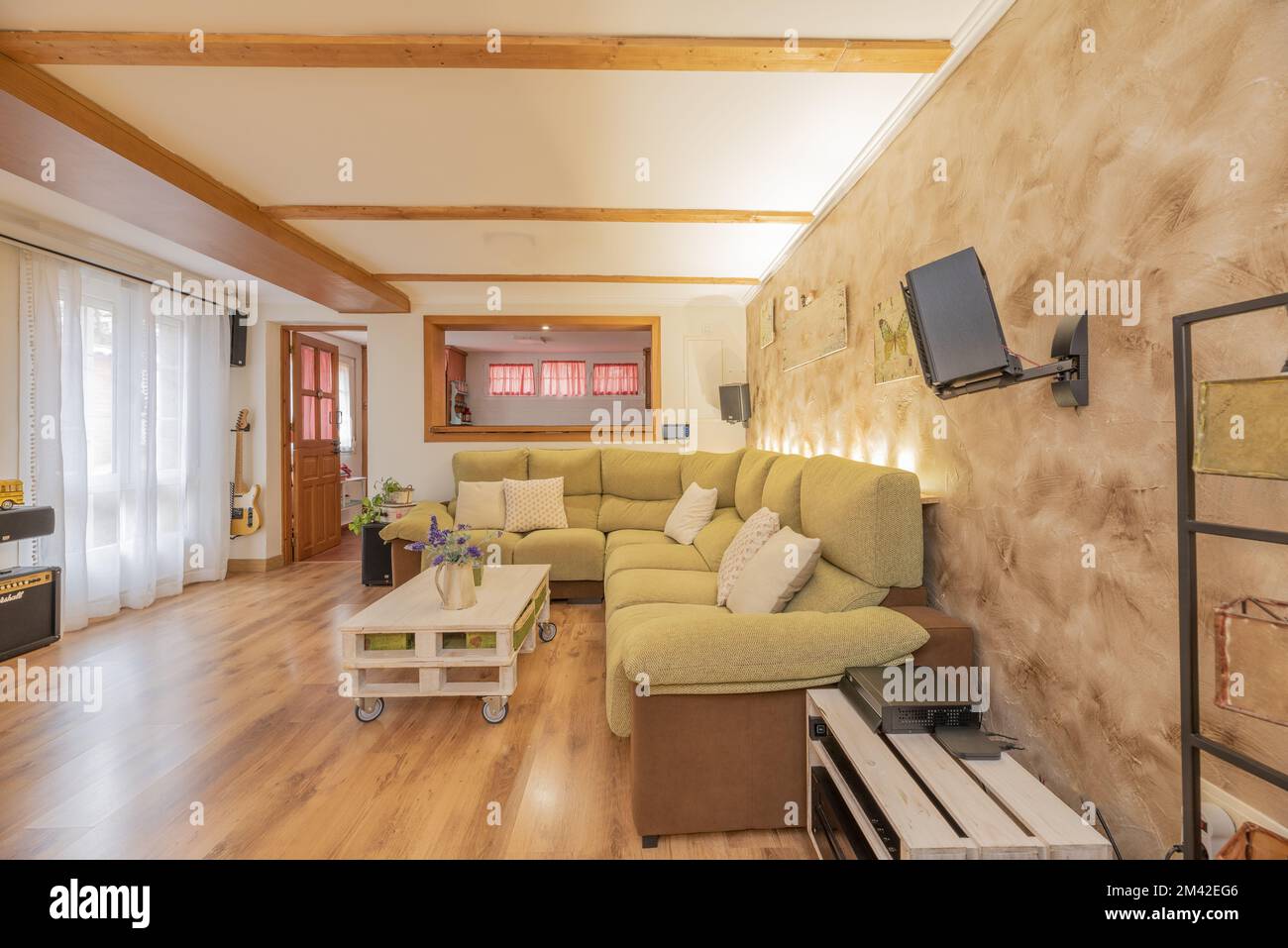 Salle de séjour avec un long canapé à deux murs tapissé de tissus verts et bruns et une table basse blanche en bois de palette Banque D'Images