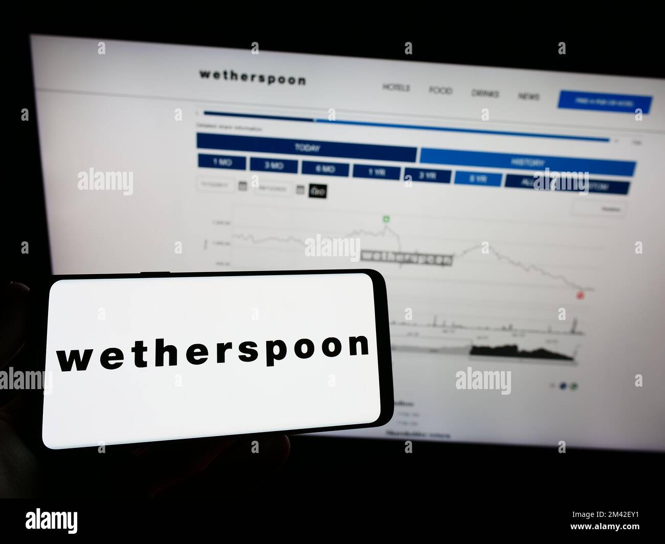 Personne tenant un téléphone portable avec le logo de la société de pub britannique J D Wetherspoon plc à l'écran en face de la page Web d'affaires. Mise au point sur l'affichage du téléphone. Banque D'Images