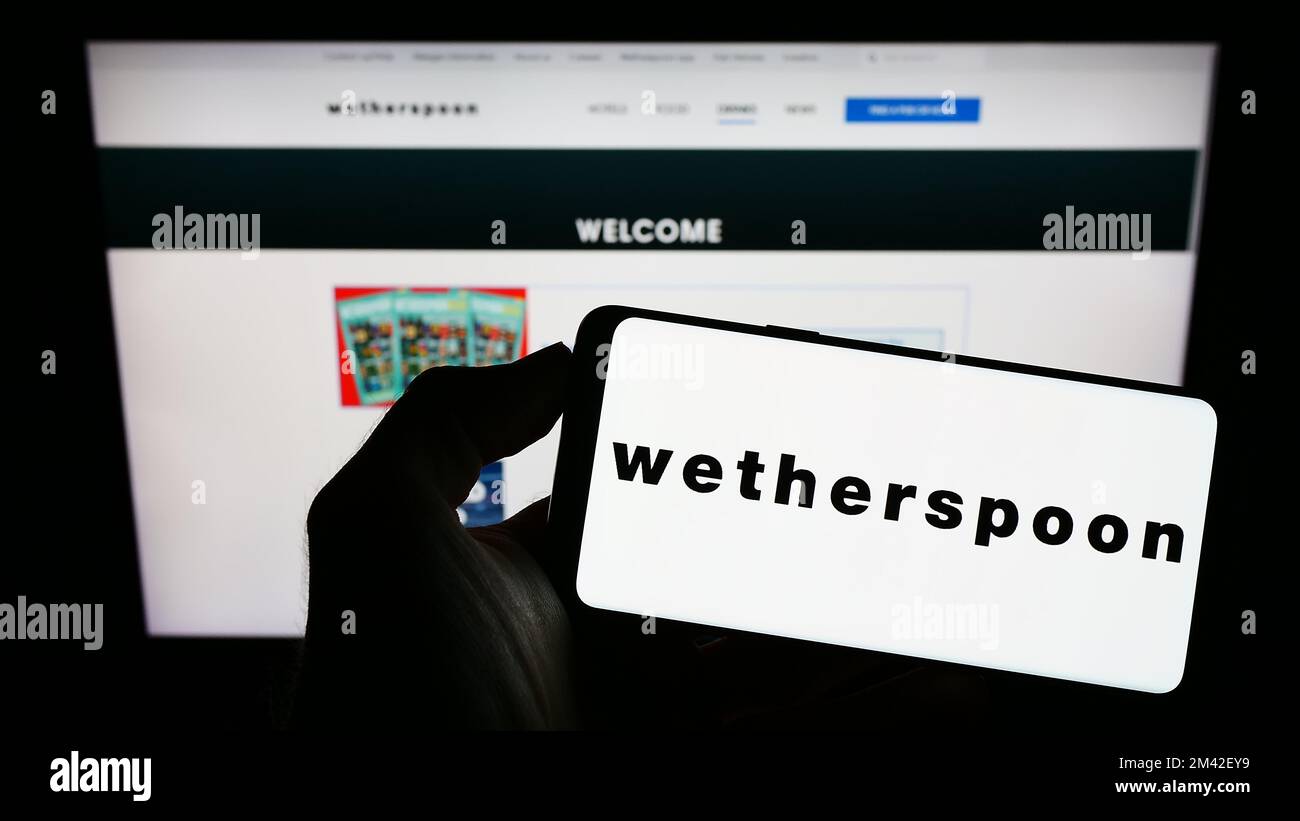 Personne tenant un smartphone avec le logo de la société de pub britannique J D Wetherspoon plc à l'écran devant le site Web. Mise au point sur l'affichage du téléphone. Banque D'Images