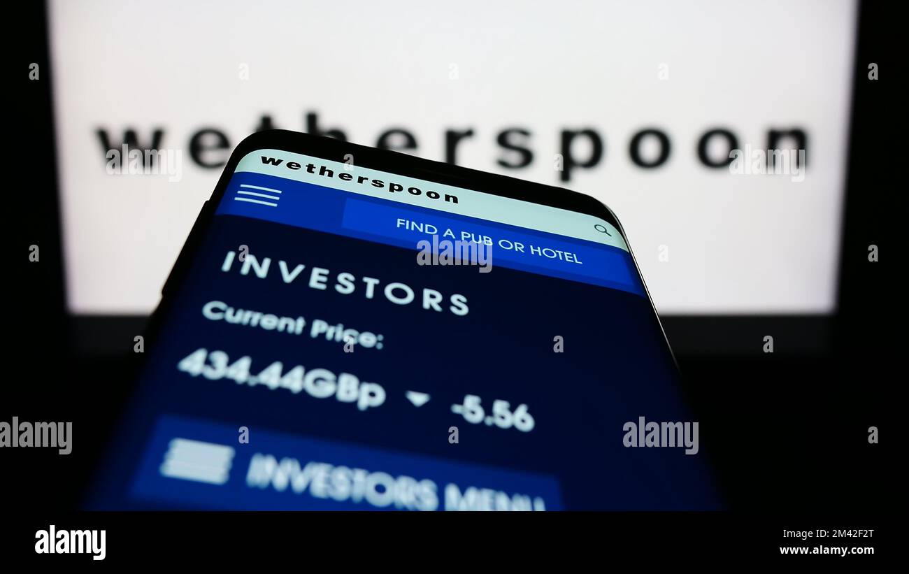 Téléphone mobile avec page Web de la société de pub britannique J D Wetherspoon plc à l'écran devant le logo de l'entreprise. Faites la mise au point dans le coin supérieur gauche de l'écran du téléphone. Banque D'Images