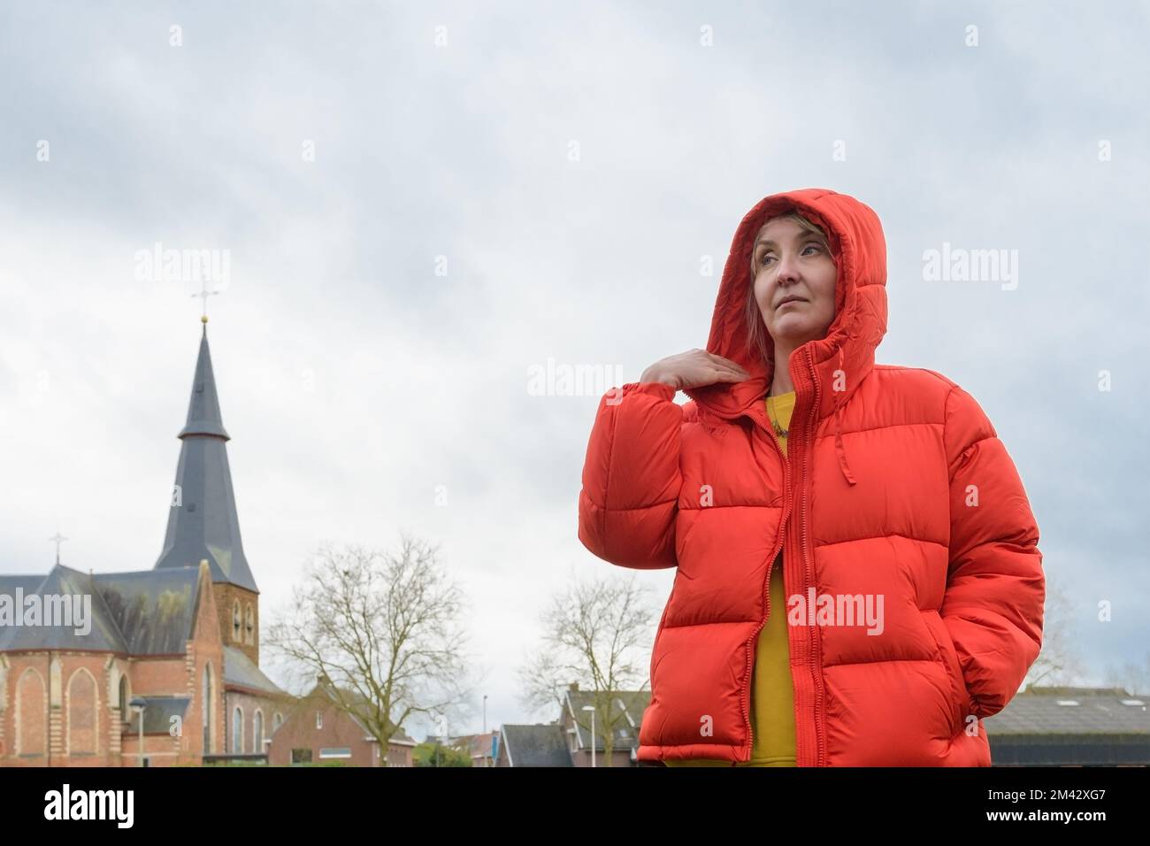 Femme dans une veste rouge. Portrait de la femme contre une vieille église catholique et ciel nuageux. copier l'espace Banque D'Images