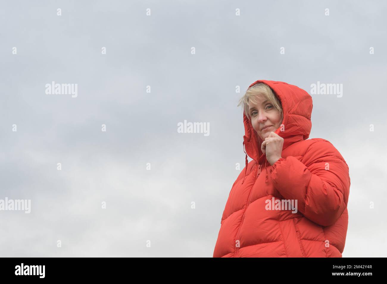 Une femme dans une veste rouge. Portrait contre un ciel nuageux. copier l'espace Banque D'Images