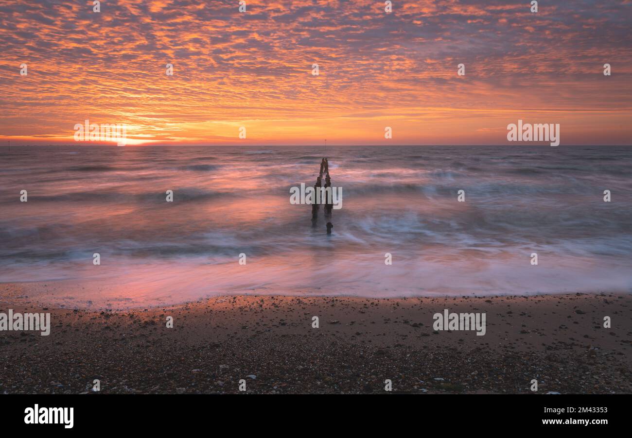 Lever de soleil sur la mer du Nord sur l'île de Mersea est dans l'Essex. Wavebreaker dans la mer longue exposition. Ciel chaud, rouge, orange et jaune le matin. Couleurs éclatantes Banque D'Images